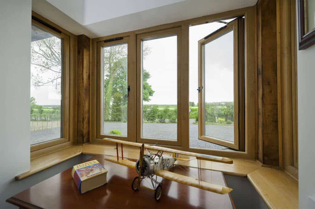 Desk with model airplane on it facing classic hardwood windows, with view of trees outside
